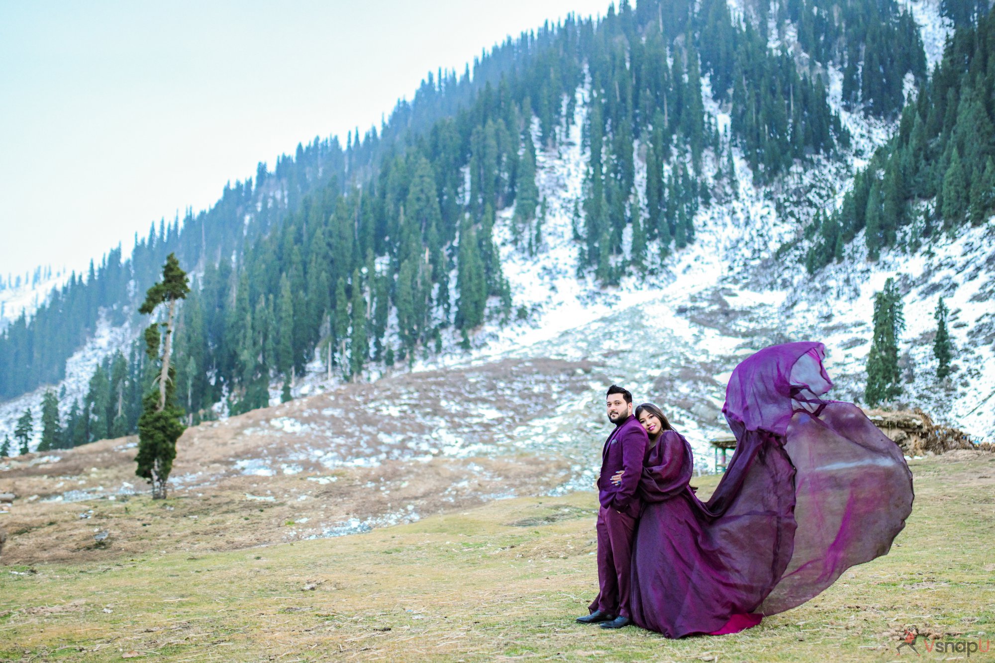 A romantic scene of a couple in traditional purple wear hugging in the snowy mountains, eyes shut, lost in their love.